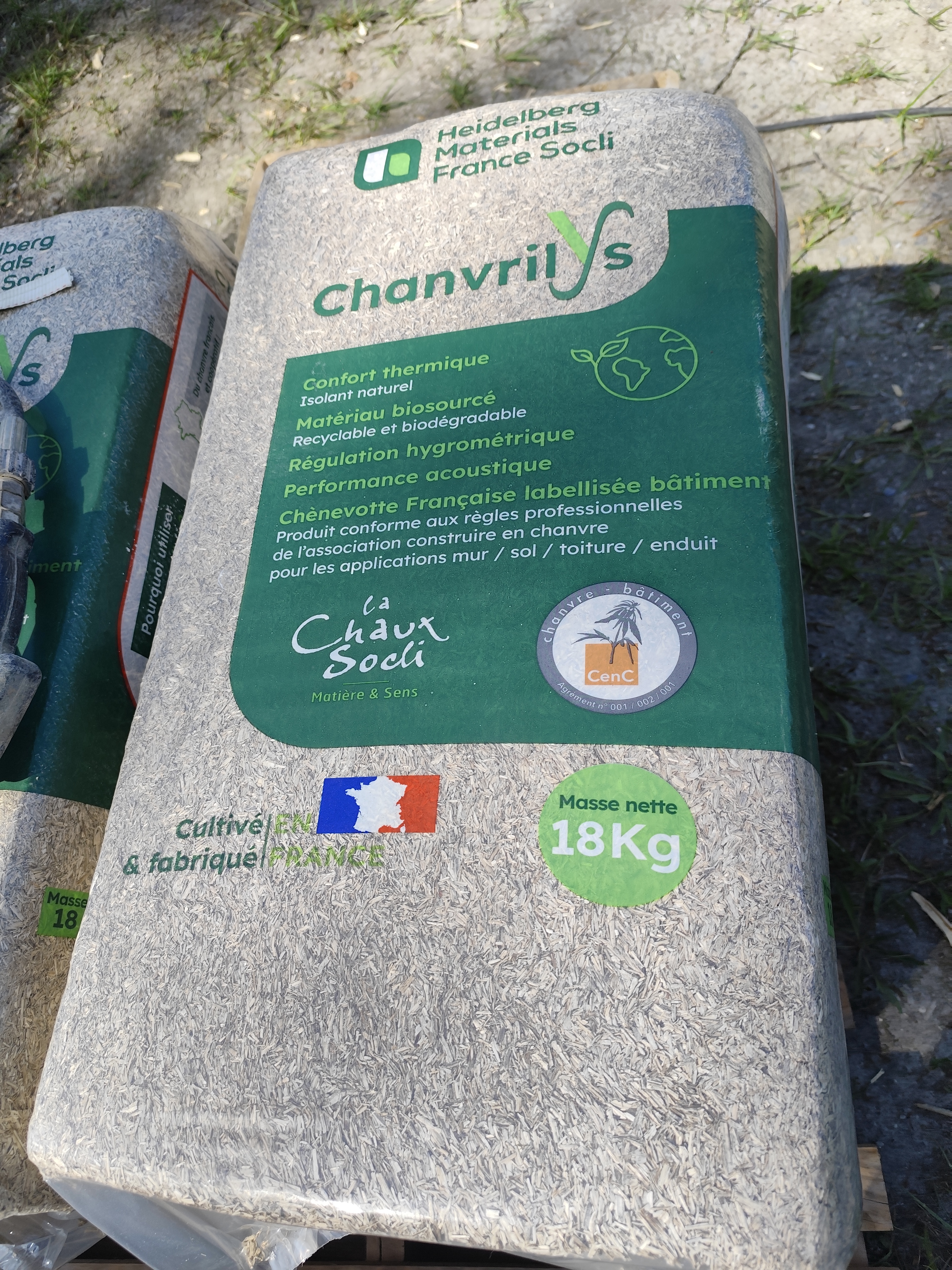 Sac de 18 kg de chanvre isolant de la marque "Chanvrilys", posé sur le sol. L'emballage vert et beige contient des informations en français, dont la composition naturelle, les avantages écologiques, et des certifications. Un logo bleu-blanc-rouge indique une fabrication française.
