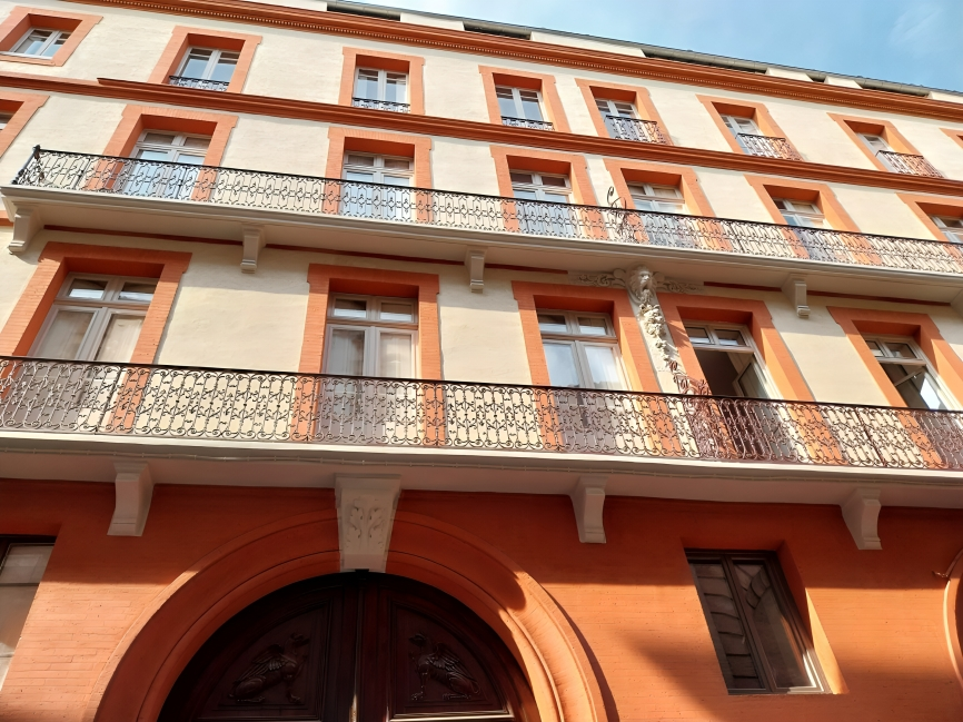 A multi-story orange and beige building with decorative balconies and large wooden doors.